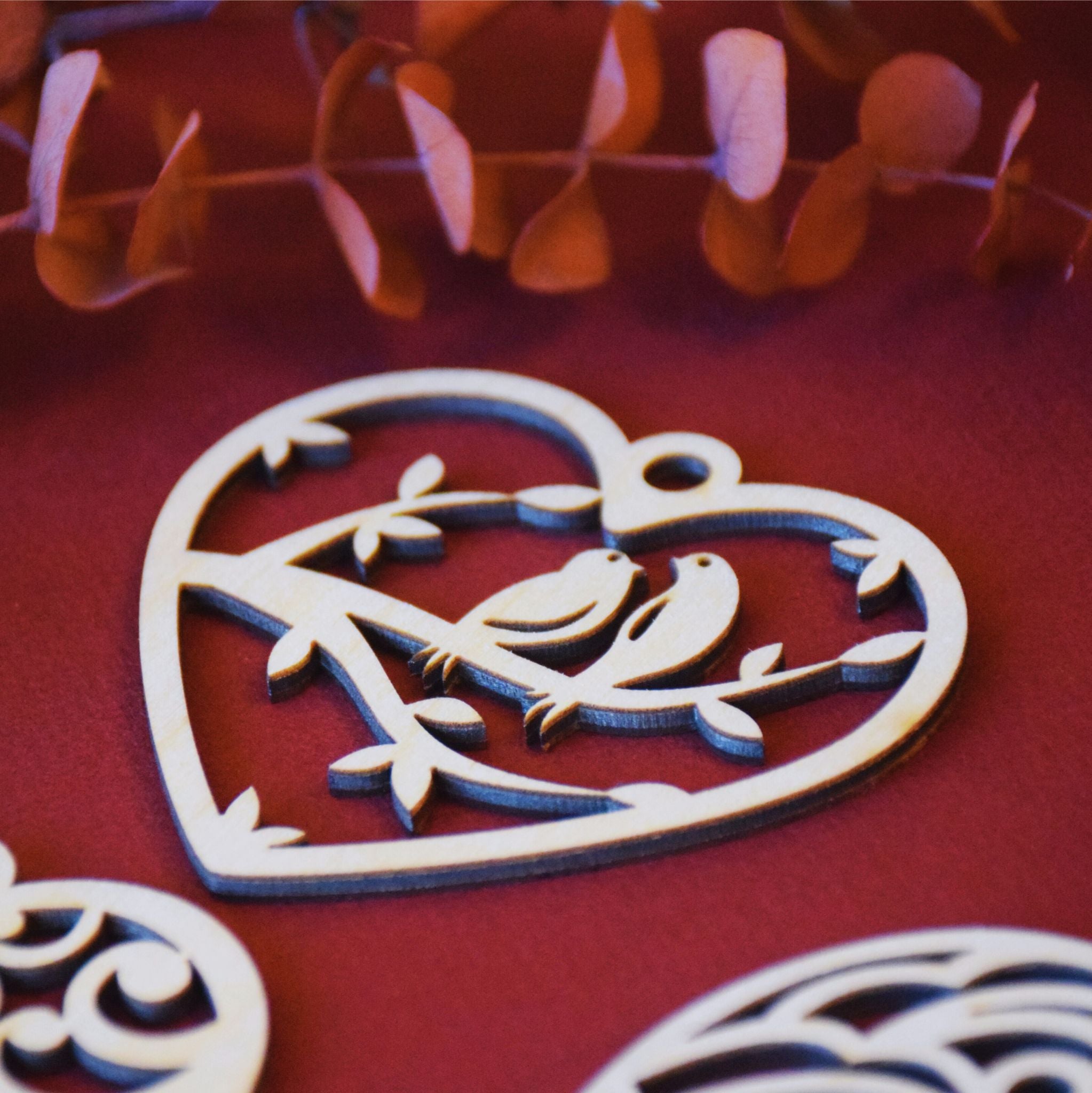 Heart ornament laying on a red background with two birds carved into birch wood