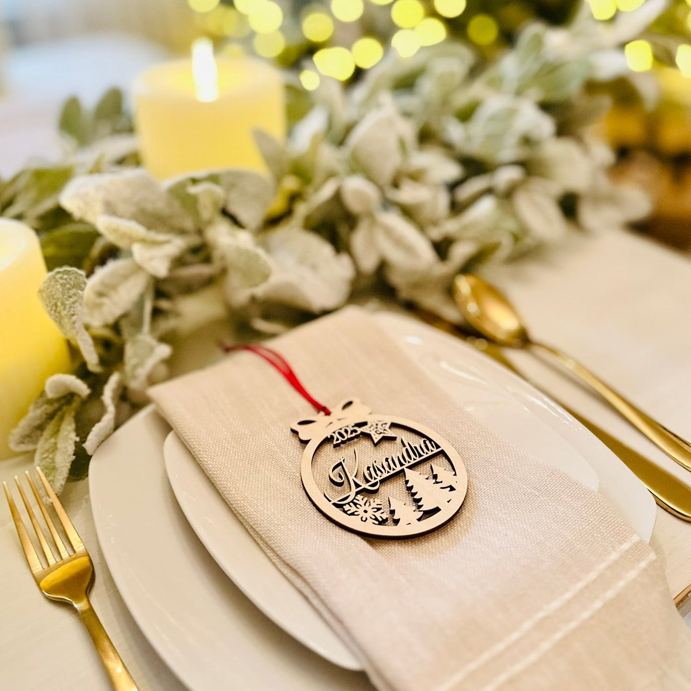 Christmas table setting with gold cutlery, white plates, and a decorative ornament on a white napkin. Personalized ornament used as a place setting name tag