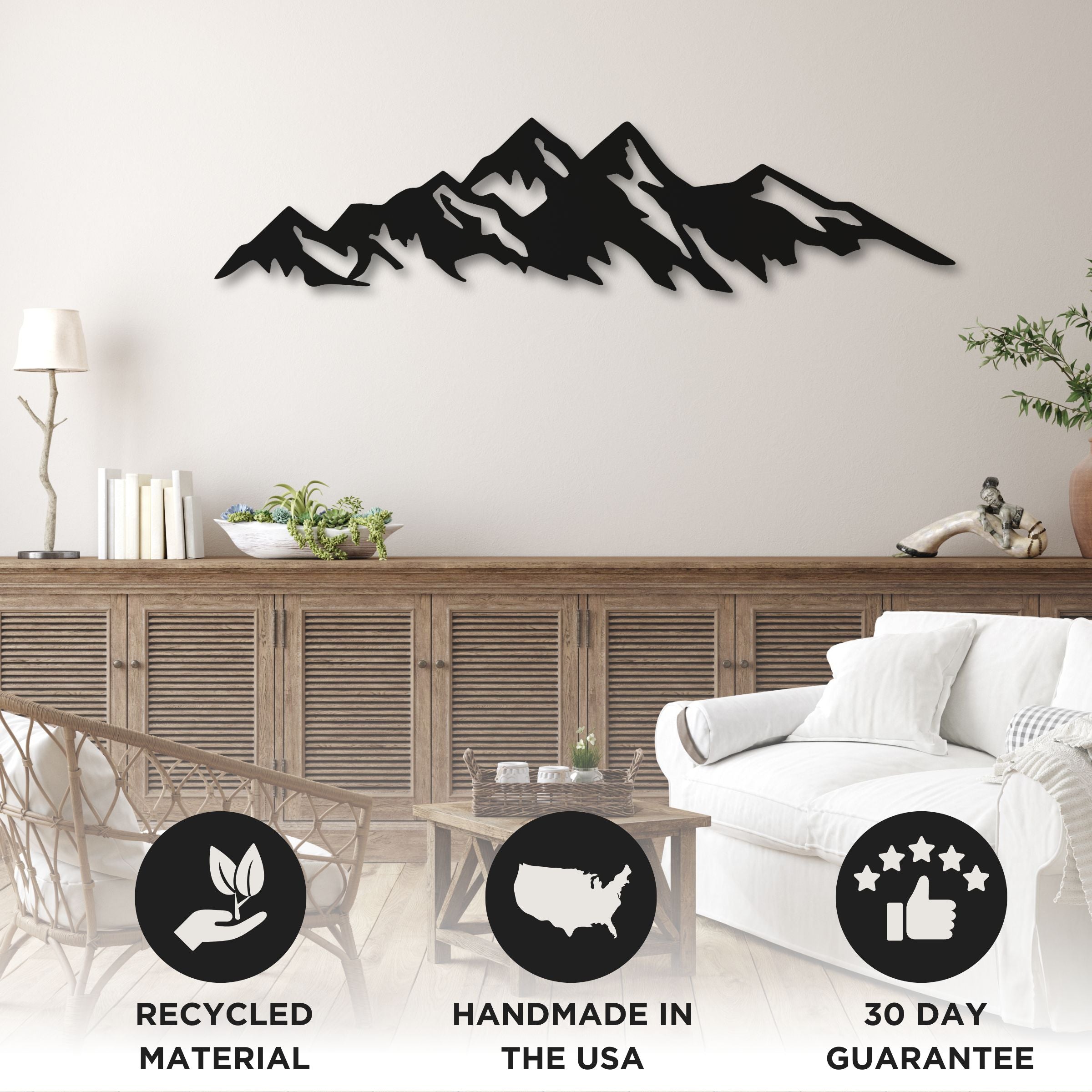 A black wood wall art depicting a mountain range placed above a wooden console table in a living room setting. There are icons indicating the material is recycled, it's handmade in the USA, and it has a 30 day guarantee.