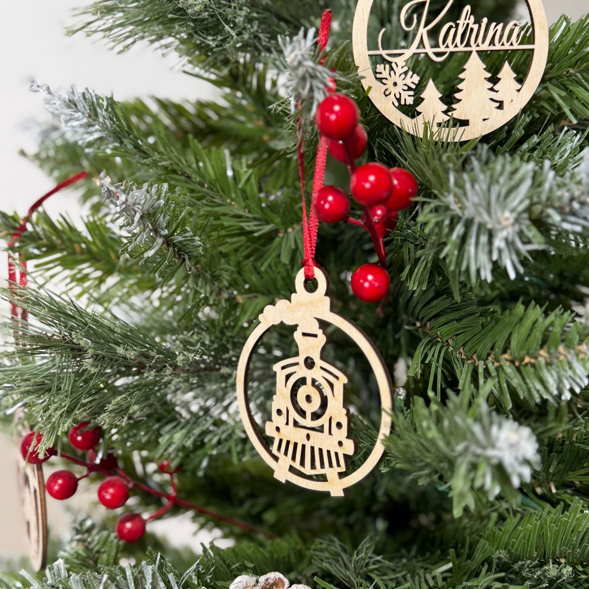 Wood vintage train ornament on a Christmas tree with red berries and a personalized wooden tag.