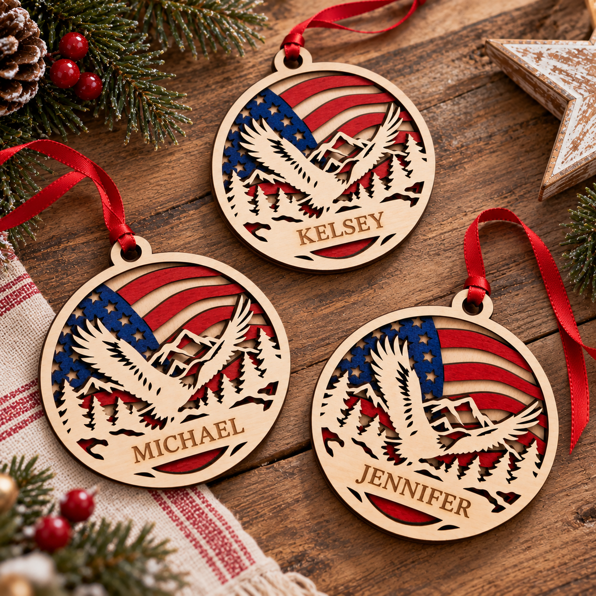 Three personalized round wooden Christmas ornaments hang on a rustic wooden surface, each featuring a laser-cut bald eagle over a mountain range and an American flag design. The names Michael, Kelsey, and Jennifer are engraved at the bottom of each ornament.