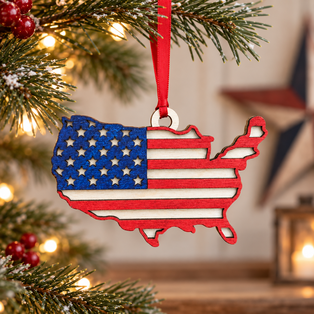 A wooden USA map Christmas ornament decorated with the American flag pattern, hanging from a red ribbon on a decorated Christmas tree branch.