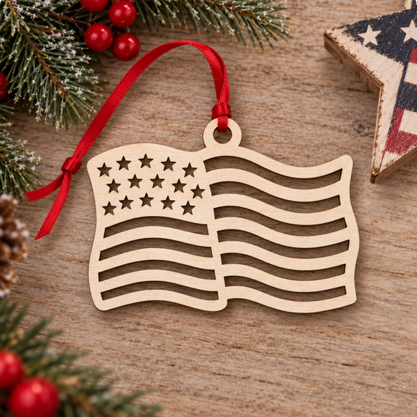 A wooden American flag ornament with a red ribbon hanger, displayed on a rustic wooden surface with holiday greenery and red berries.
